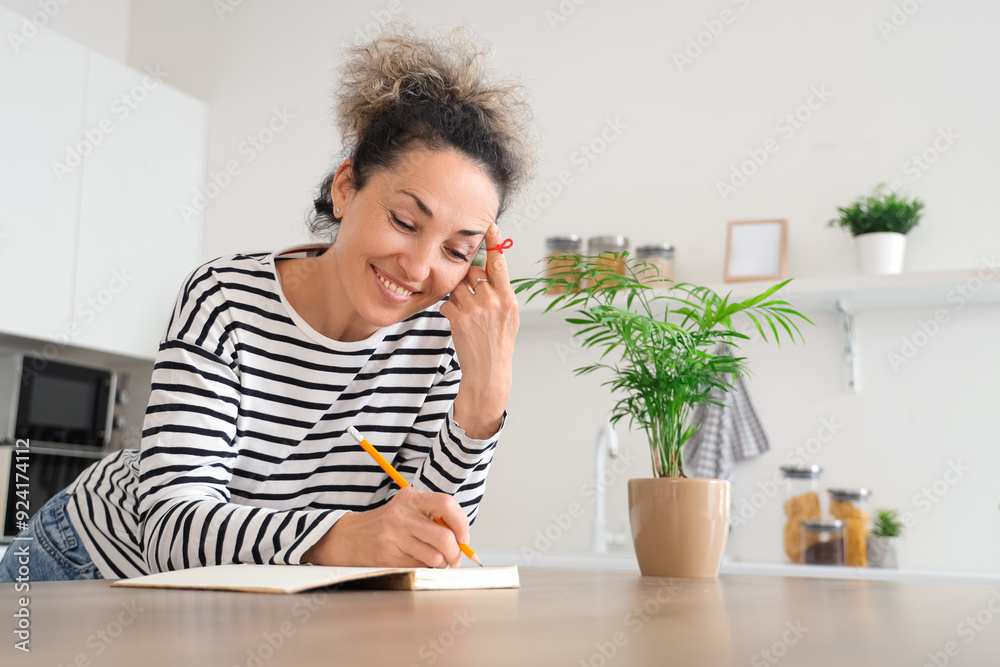 Beautiful middle-aged woman with red string on her finger writing something in notebook at home. Reminder concept Beautiful middle-aged woman with red string on her finger writing something in notebook at home. Reminder concept