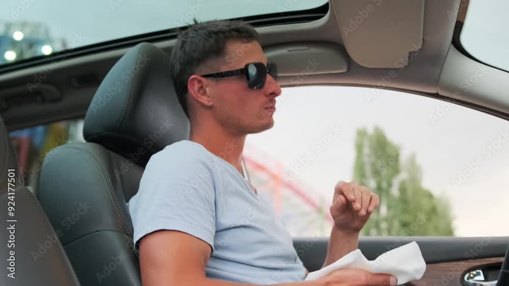 Handsome guy snacking on french fries holding fast food in napkin sitting behind the wheel of car waiting in parking lot. Handsome guy snacking on french fries holding fast food in napkin sitting behind the wheel of car waiting in parking lot.