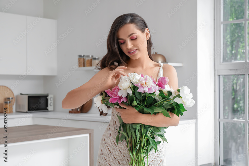 Beautiful young woman with bouquet of peony flowers in kitchen Beautiful young woman with bouquet of peony flowers in kitchen