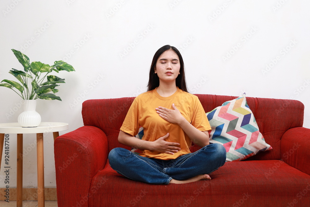 Asian Woman sitting on couch and doing calming breathing exercises. Female inhaling and exhaling to deep breath. Concept of mental health. Asian Woman sitting on couch and doing calming breathing exercises. Female inhaling and exhaling to deep breath. Concept of mental health.