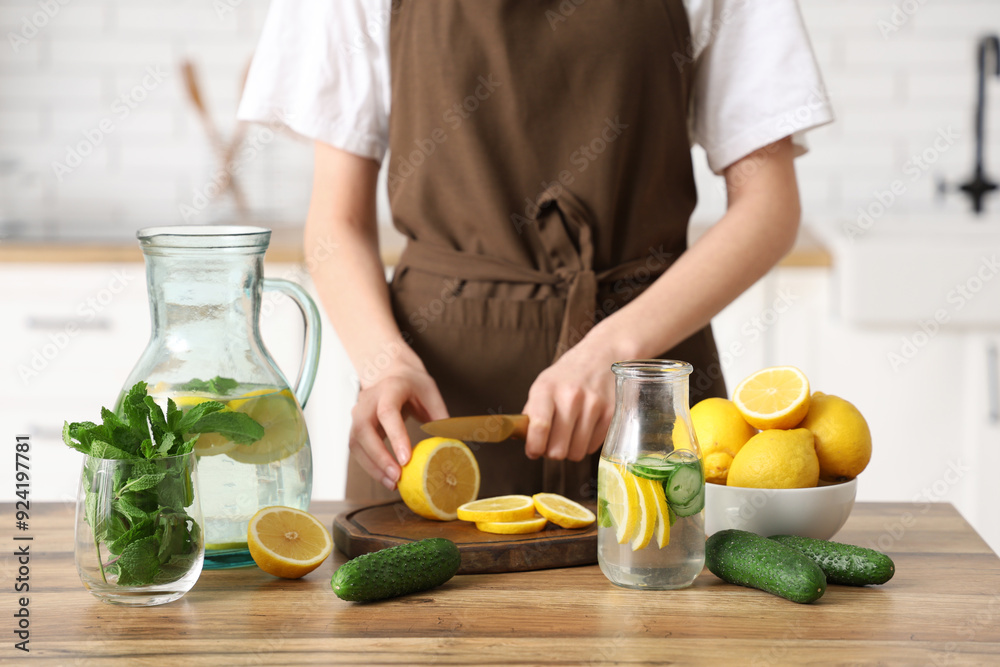Young woman cutting lemon for preparing infused water with mint in kitchen Young woman cutting lemon for preparing infused water with mint in kitchen