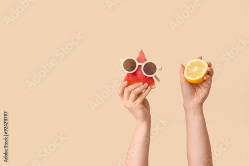 Female hands with piece of sweet watermelon, sunglasses and lemon on beige background