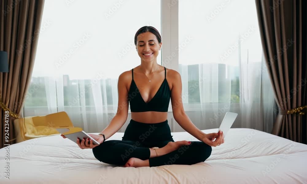 Smiling businesswoman put off laptop computer and taking yoga lotus position sitting relaxed on bed in hotel room. Travel, business and people concept