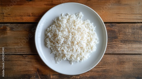 A top-down shot of perfectly steamed Thai Jasmine rice on a white plate, placed on a rustic wooden background. Clean and appetizing.