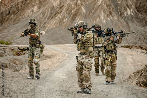 A group of military men in combat gear patrol in the middle of a desert and tropical jungle. Soldiers in full combat gear in dry weather conditions assemble and march on a mission.