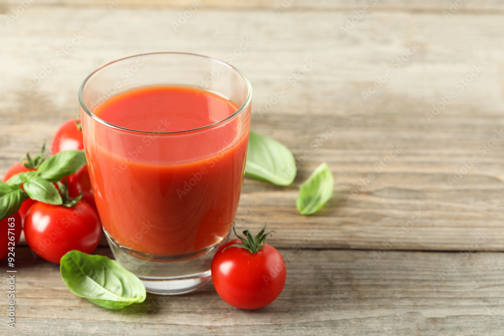 Tasty tomato juice in glass, basil leaves and fresh vegetables on wooden table, space for text Tasty tomato juice in glass, basil leaves and fresh vegetables on wooden table, space for text