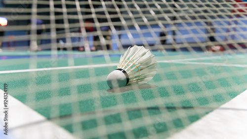 The shuttlecock lies on the ground on the green badminton court. Background taken in low light