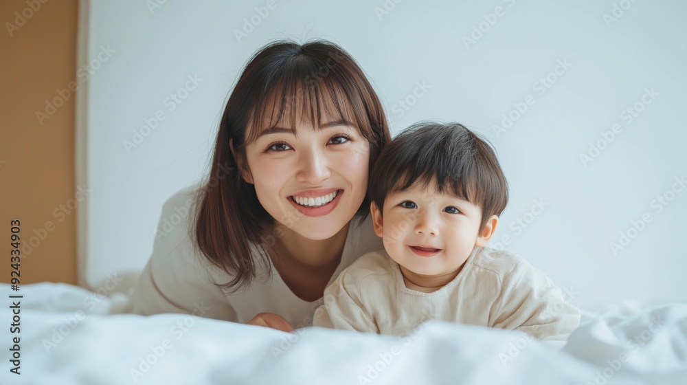 A mother and her young child smiling together on a bed in a bright, cozy room. A mother and her young child smiling together on a bed in a bright, cozy room.