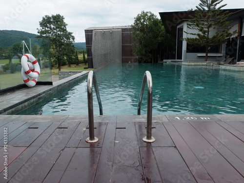 symmetry shape of outdoor swimming pool ladder in front of the blue water in the hotel with the mountain in the background.