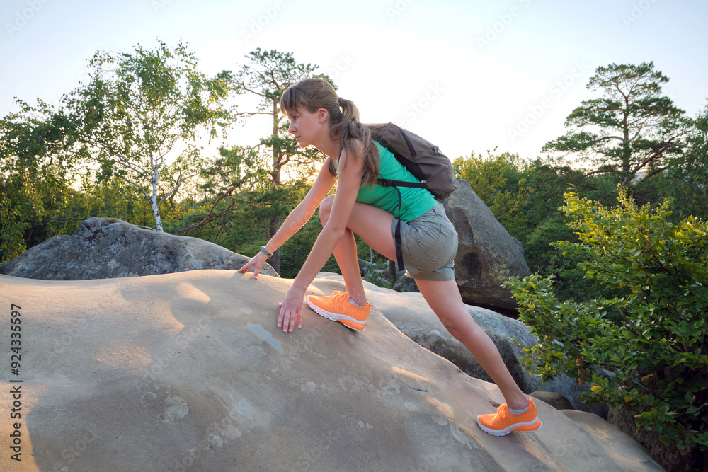 Obraz premium Hiker woman clambering on rocky mountain footpath in evening nature. Lonely female traveler traversing hard wilderness trail. Healthy lifestyle and sport concept