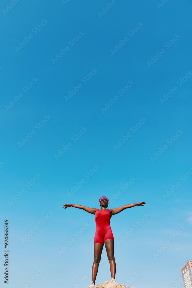 Woman in a red swimsuit poses confidently on a rock against a clear blue sky Woman in a red swimsuit poses confidently on a rock against a clear blue sky