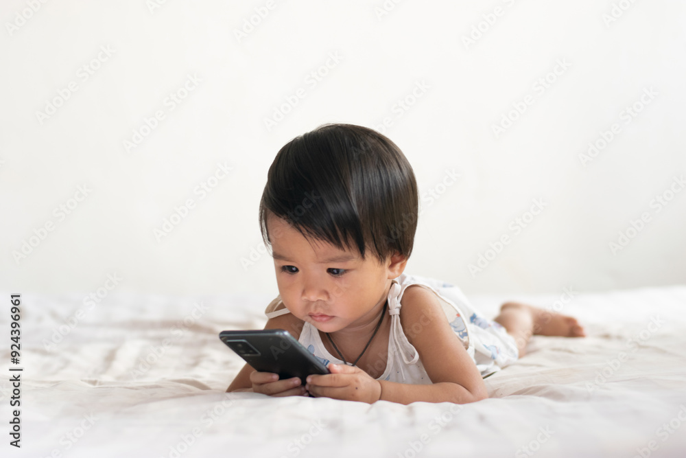 Children, cute Asian women Lie down and look at your mobile phone on the bed in the house. Children, cute Asian women Lie down and look at your mobile phone on the bed in the house.