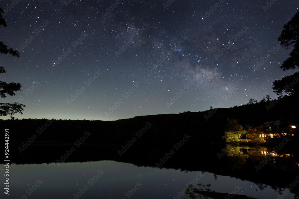 山奥の森の池に映る家の灯と水面の星と天の川