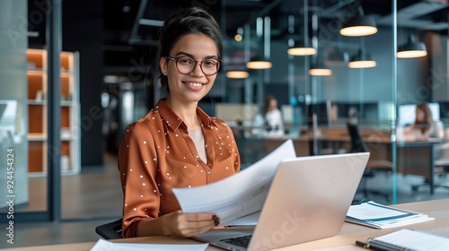 A professional female is sitting at an office desk, using the laptop to work on documents