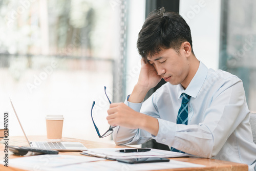 The Weight of Responsibility: A businessman, burdened by stress, sits at his desk with a furrowed brow and hand on his temple, his glasses resting nearby. The image conveys the challenges and pressure