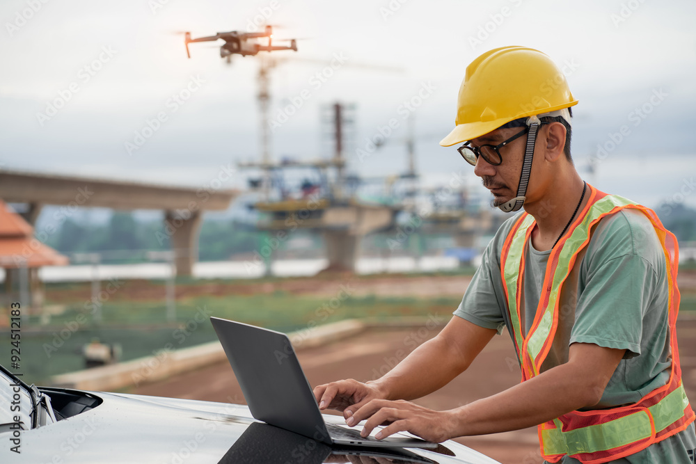 Asian male engineer using laptop and drone to inspect construction at bridge construction site. Construction area of large bridge connecting road across river. Asian male engineer using laptop and drone to inspect construction at bridge construction site. Construction area of large bridge connecting road across river.