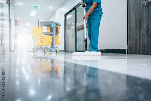 A Safety sign with caution phrase. Happy young housekeeper mopping the floor with a mop and cleaning products to clean dust in a hospital corridor.