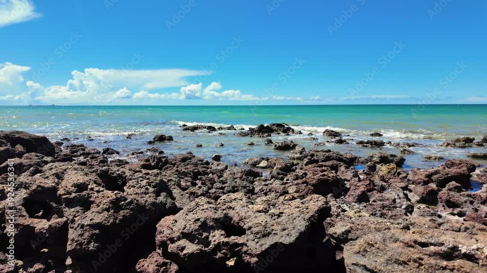 Rocky Shoreline with Clear Blue Sky and Turquoise Ocean Waters on a Sunny Day, Featuring Volcanic Rocks and Gentle Waves