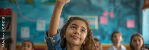 A young student in a classroom raises her hand confidently to ask a question, demonstrating engagement and eagerness to learn. photo