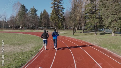 Drone Following Two Athletes Running Together on Stadium Track During Sunny Winter Day. Concept of Healthy Lifestyle, Friendship, Wellbeing, Fitness, Workout, Physical Activity, energy, Training photo