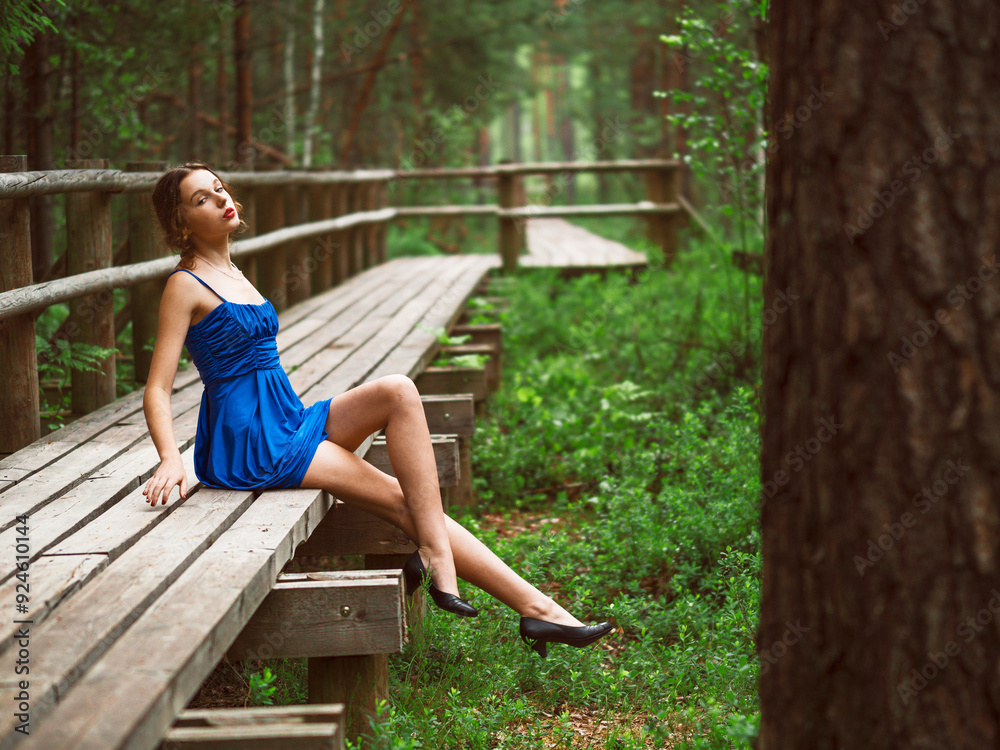 Young teenager girl in high fashion blue dress posing in a forest park. Prom photo shoot. Model short hair and slim body type. Selective focus. Young teenager girl in high fashion blue dress posing in a forest park. Prom photo shoot. Model short hair and slim body type. Selective focus.