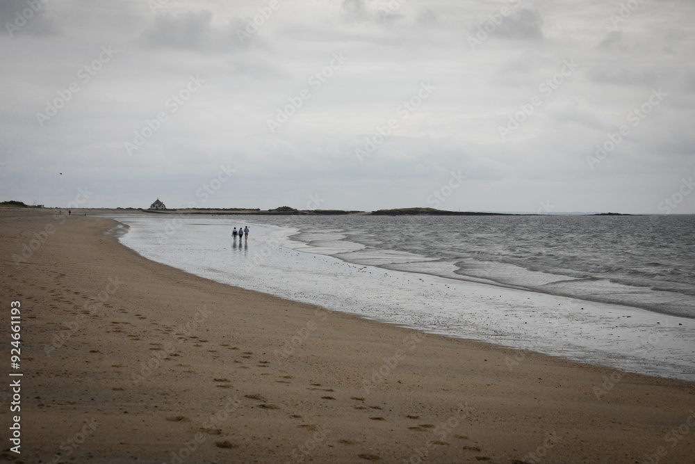 Seaside landscape on an overcast day. A large sandy bay with a chapel and rocks at the far end. Seaside landscape on an overcast day. A large sandy bay with a chapel and rocks at the far end.