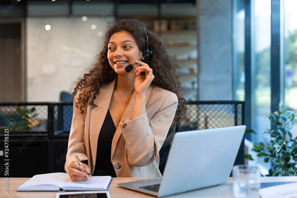 Beautiful smiling call center worker in headphones is working at modern office Beautiful smiling call center worker in headphones is working at modern office