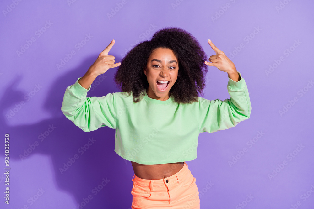 Portrait of energetic young funky hipster woman wearing green stylish top brutal rock roll fan isolated on purple color background Portrait of energetic young funky hipster woman wearing green stylish top brutal rock roll fan isolated on purple color background