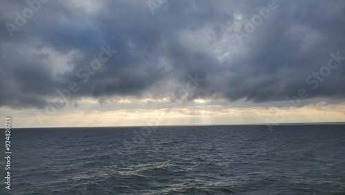 A serene seascape under a brooding sky, where rays of light pierce through clouds to touch the ocean, creating a tranquil and mesmerizing scene.