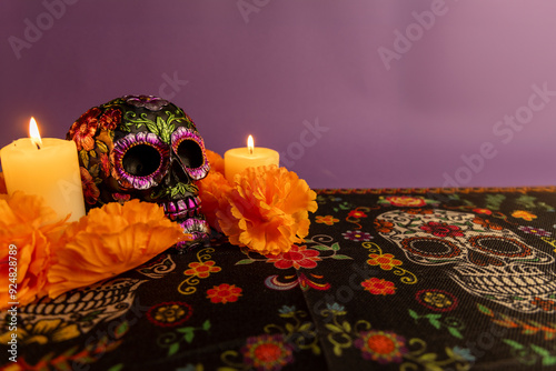 A skull with metal flower decorations and two glowing candles beside it. Orange flowers are scattered around photo