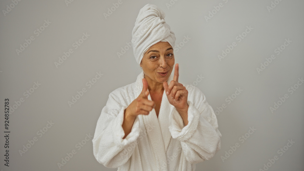 Mature woman in a bathrobe with a towel on her head pointing at the camera isolated on a white background Mature woman in a bathrobe with a towel on her head pointing at the camera isolated on a white background