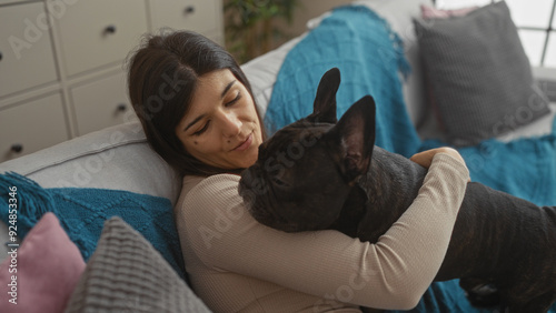 A young hispanic woman cuddles her french bulldog in a cozy living room.