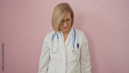 Beautiful mature blonde woman doctor wearing glasses and a stethoscope over a white coat, isolated against a pink background. photo