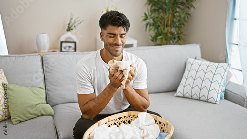 Fotografi Handsome hispanic man enjoying the fresh scent of clean laundry in a cozy living room