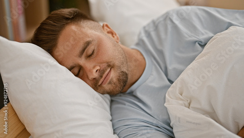 Handsome young man sleeping peacefully in a bright bedroom interior with blue bedding.