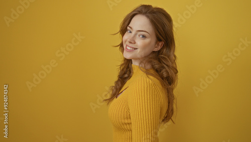 A beautiful young woman with blonde hair smiles while standing over an isolated yellow background wall, showcasing her vibrant style and cheerful demeanor.