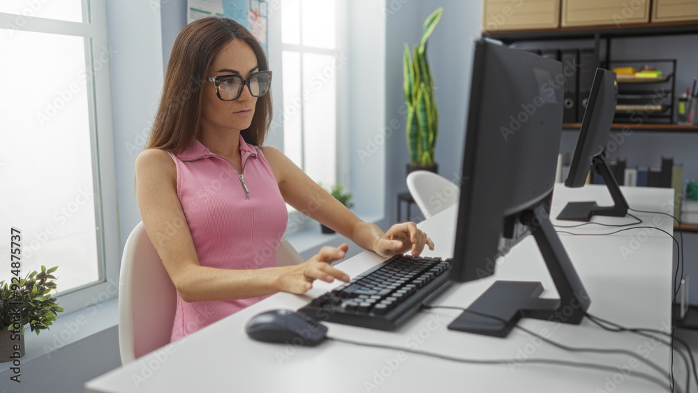Woman working on computer in modern office wearing glasses and pink top, focused and professional, surrounded by plants and office furniture, bright window light, indoor setting Woman working on computer in modern office wearing glasses and pink top, focused and professional, surrounded by plants and office furniture, bright window light, indoor setting