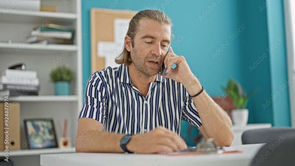Fototapeta premium Handsome middle-aged man with long hair talking on the phone in a modern office.