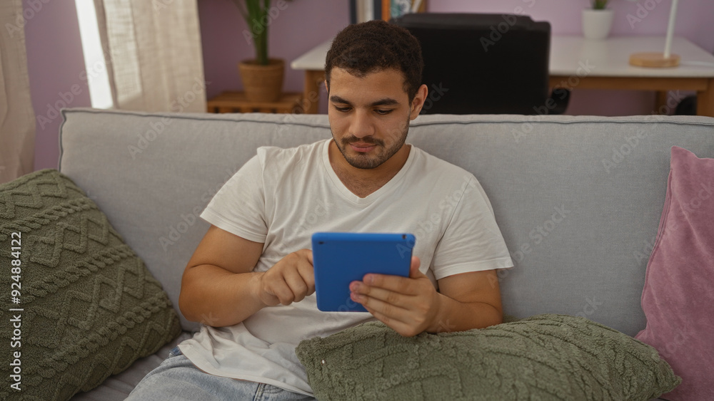 Young hispanic man using tablet indoors in a cozy living room Young hispanic man using tablet indoors in a cozy living room
