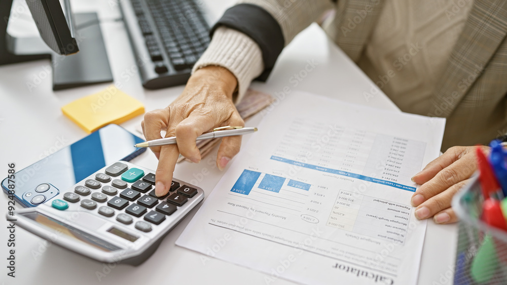 Mature hispanic woman working with calculator and financial documents at her office desk Mature hispanic woman working with calculator and financial documents at her office desk