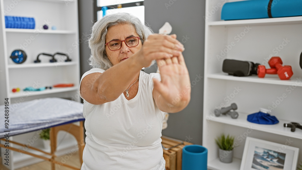 Mature woman stretching hands in a rehab clinic's indoors gym, suggesting health, recovery, exercise, and well-being. Mature woman stretching hands in a rehab clinic's indoors gym, suggesting health, recovery, exercise, and well-being.