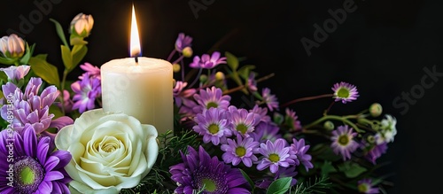 Purple and white flowers arranged with a glowing white candle symbolizing sympathy and condolences set against a black background with copy space image