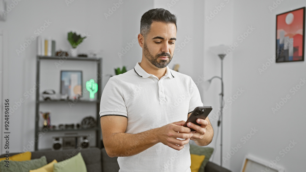Hispanic man with beard using smartphone in modern living room Hispanic man with beard using smartphone in modern living room
