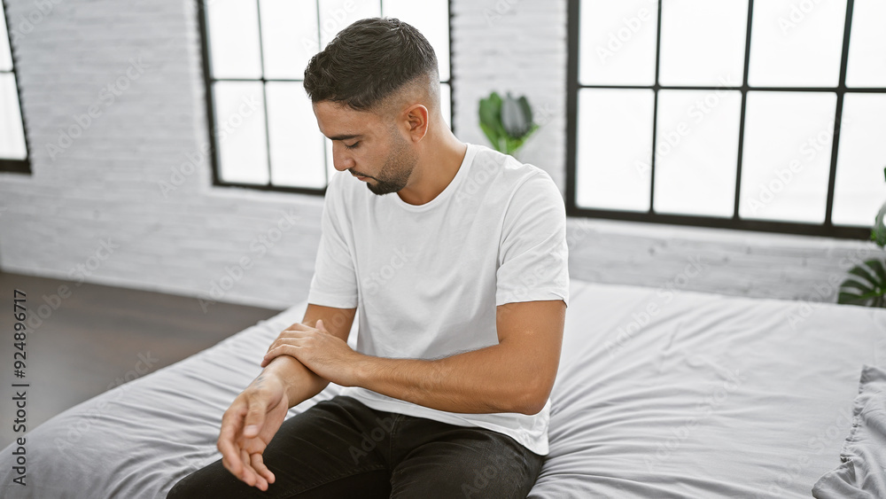 Handsome bearded man sitting thoughtfully on bed in a minimalist bedroom.