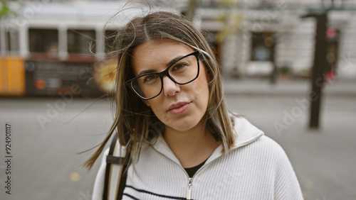 Close-up of a thoughtful young woman with glasses on a budapest street, tram blurred in the background.