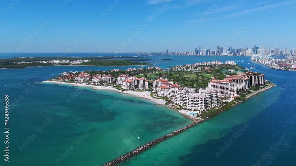 View of coastal area known as South Point. Series of red-roofed buildings on peninsula surrounded by turquoise waters with city skyline in distance and clear blue skies above View of coastal area known as South Point. Series of red-roofed buildings on peninsula surrounded by turquoise waters with city skyline in distance and clear blue skies above