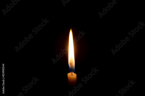 A single burning candle flame or light glowing on a white candle on black or dark background on table in church for Christmas, funeral or memorial service with copy space