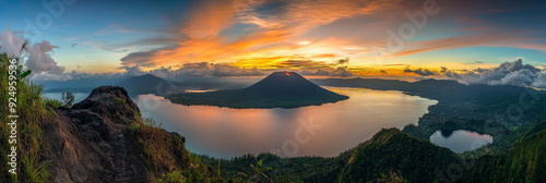 Breathtaking Sunrise over Volcanic Island and Lake in Indonesia - A panoramic view of a volcanic island in a serene lake at sunrise. The sky is ablaze with vibrant colors, reflecting on the calm water