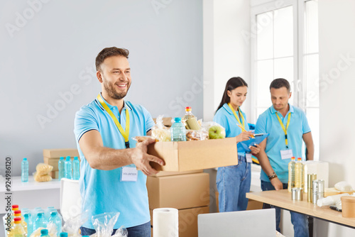 Smiling man volunteer holding a box of foodstuffs while working at a humanitarian aid center. His charity work and dedication to providing help and support demonstrate donation service. photo