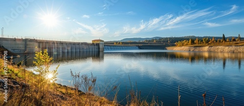 Sunny day with clear blue sky over a water reservoir featuring a dam wall and a building ideal for copy space image